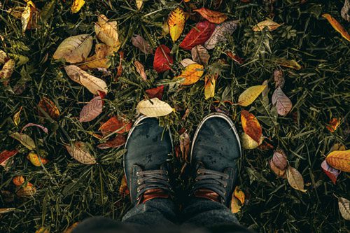 man's feet standing on grass with fall colored leaves - thanksgiving