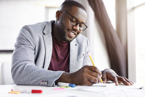 handsome African American man smiling and making notes in planner or notebook - goals