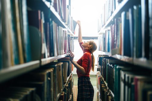 woman reaching for book on library shelf - ideas