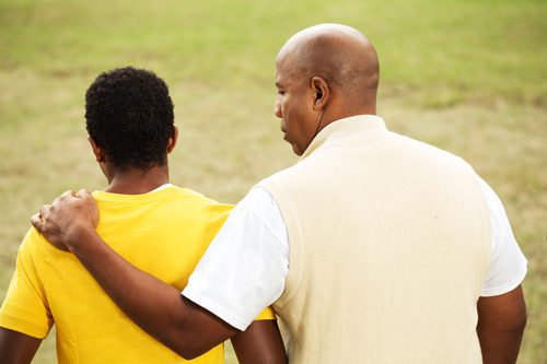 African American dad with arm around teenage son - view from behind them - teen
