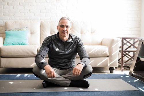 middle age man sitting on exercise mat at home - exercise