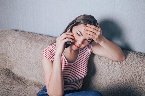 young woman looking stressed using cell phone sitting on couch at home - time to enter recovery