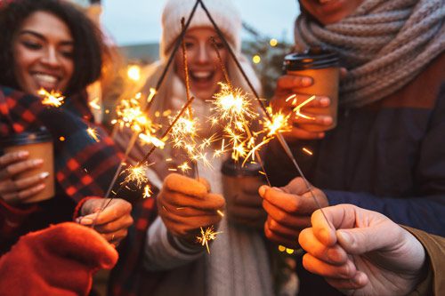 young adult friends using sparklers outdoors in cold weather - holiday season