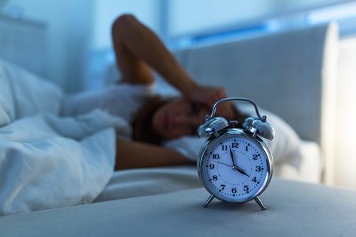 woman suffering from insomnia laying awake in bed with alarm clock showing 4 - Ambien addiction