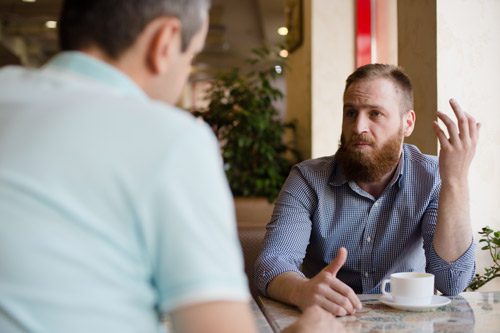 handsome bearded man with red hair having serious conversation in cafe with other man - 12-Step sponsor
