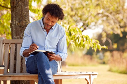 man sitting outside on a bench writing in a notebook - journaling prompts