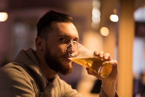 handsome man in his thirties drinking from a pint glass at a bar, looking at the camera - social anxiety disorder